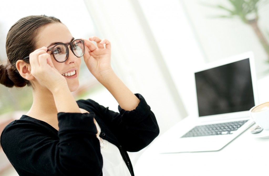 Young businesswoman adjusting her glasses as she prepares to start working on her laptop computer on her desk